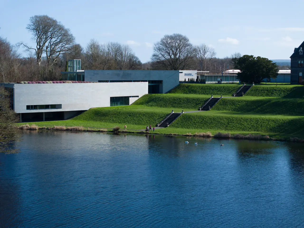 A modern museum building set into a lawn beside a lake
